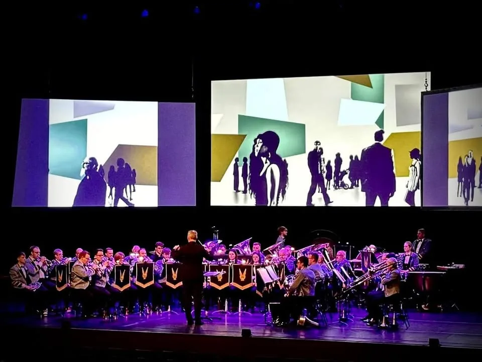 The KNDS Fairey Band performing beneath three screens of synchronised animation at Perth Concert Hall